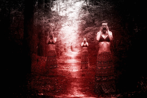 Τρεις γυναίκες μάγισσες στέκονται στις αντίθετες πλευρές ενός δασικού μονοπατιού, σε μια φεγγαρόλουστη νύχτα, σκεπάζοντας τα μάτια τους με τα χέρια τους και φωνάζοντας, με κόκκινο φως αίματος, την έννοια του αποκριάτικου τρόμου και φόβου - Φωτογραφία, εικόνα