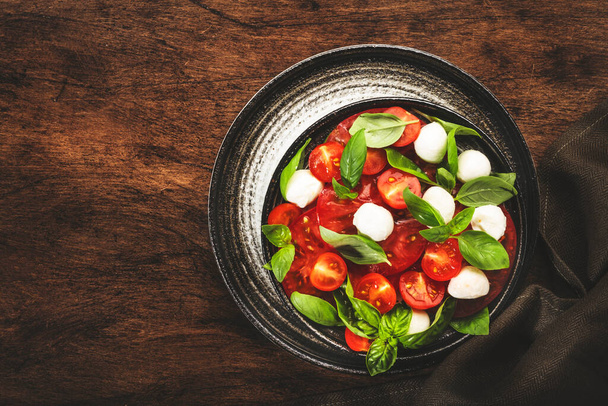 Caprese salad with ripe red tomatoes and mozzarella cheese with fresh green basil leaves. Italian food. Top view, wooden background - Foto, Imagem