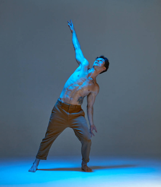 Cool young man dancing expressive dance without shirt in neon light in studio. Dance school poster. Body with tattoos - Zdjęcie, obraz