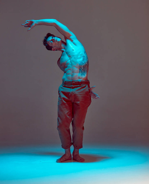 Handsome man dancer without shirt dances in neon light in studio. Dance school poster. Body with tattoos - 写真・画像