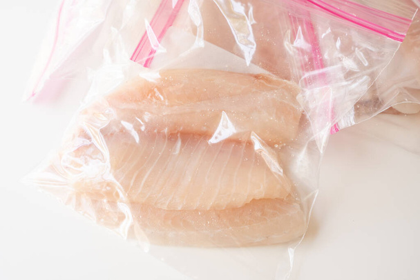 Φιλέτο φρέσκου ωμού ψαριού σε σακούλες με φερμουάρ. Φιλέτο Tilapia σε λευκό τραπέζι κουζίνας, με θέα από ψηλά - Φωτογραφία, εικόνα
