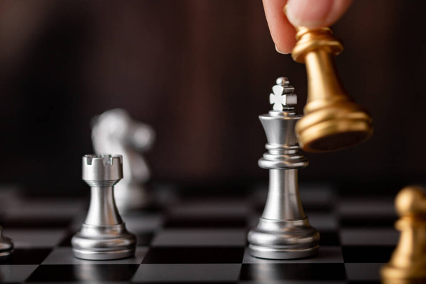 mano sosteniendo oro rey ataque plata líder en juego en el tablero de ajedrez - Foto, Imagen