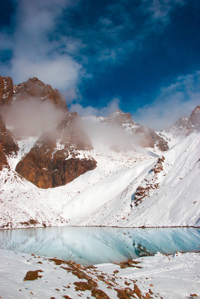 The mountain lake is surrounded by snow peaks. Mountains behind clouds. - Photo, Image