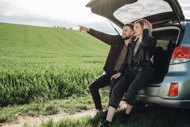 Happy Young Traveler Couple Dressed Alike in Black Leather and Jeans Jacket Having Fun Time on Road Trip in Green Field - Photo, Image