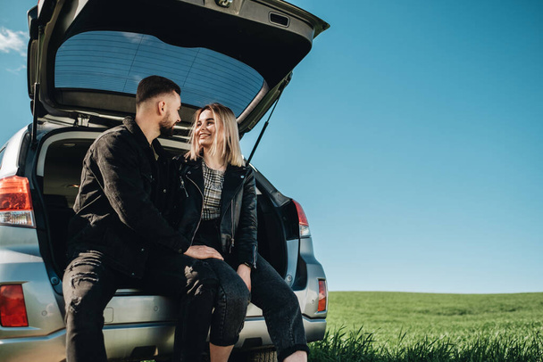 Feliz joven viajero pareja vestida como en cuero negro y Jeans chaqueta divertirse tiempo en viaje por carretera en Green Field - Foto, imagen
