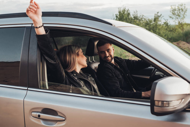 Jovem viajante feliz casal vestido igual em couro preto e jaqueta de jeans se divertindo na viagem de carro fora da cidade
 - Foto, Imagem