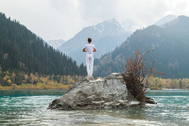A man in a Samasthiti pose on a stone among a mountain lake. - Photo, Image