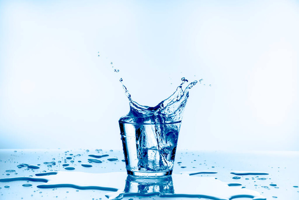 Jég esett az üvegbe, víz fröccsent üveg elszigetelt kék háttér - Fotó, kép