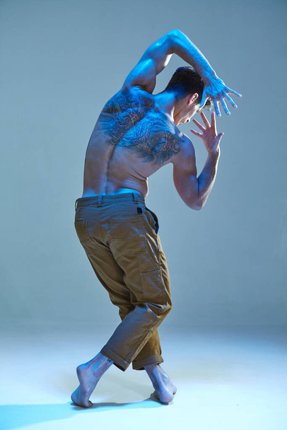 Cool young man dancer without shirt in neon light. Dance school poster. Body with tattoos. View from back - Φωτογραφία, εικόνα