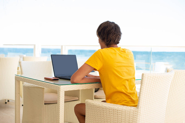 Local de trabalho em um café com vista para o mar. Um homem a trabalhar num portátil num café. Espaço de cópia, Mock up. - Foto, Imagem