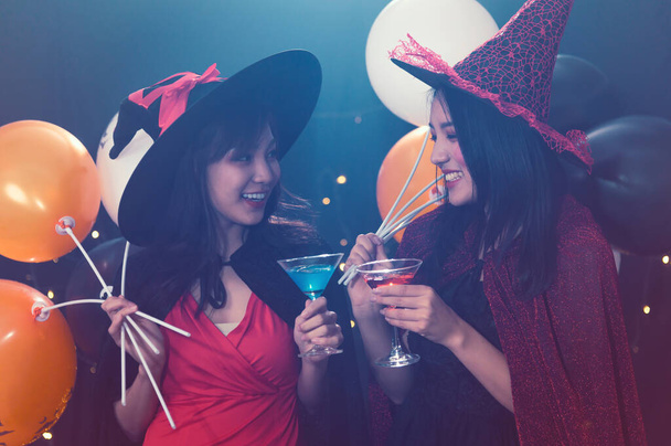 Porträt von zwei schönen jungen Frauen in Hexenkostümen auf einer Party vor dunklem magischen Hintergrund - Konzept für eine Halloween-Party - Foto, Bild