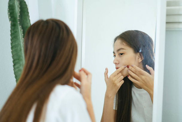 Long hair woman squeeze an acne in front of big mirror near by giant cactus. - Photo, image