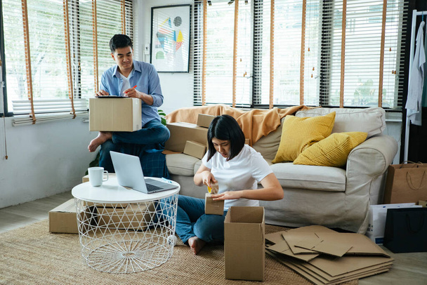 Mann und Frau sitzen im Wohnzimmer und verpacken die Waren als Online-Bestellung. - Foto, Bild