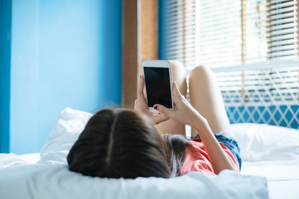 Dlouhé vlasy žena ležet na posteli v dopoledních hodinách a nakupování online se svým smartphonem. - Fotografie, Obrázek