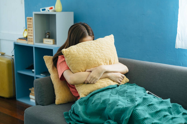 Długie włosy kobieta siedzi na kanapie w salonie z zielonym kocem przytulić żółtą poduszkę, podczas gdy jej sklep internetowy nie może zarobić, więcej nad sklepem jest w czerwonym. - Zdjęcie, obraz