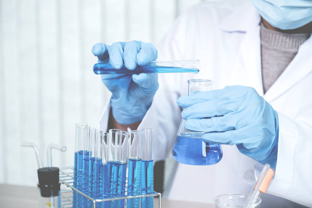 Os cientistas possuem um tubo de vidro cheio de líquido químico azul para pesquisa e análise em laboratório. - Foto, Imagem