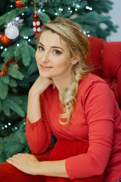 Όμορφη νεαρή ξανθιά γυναίκα με κόκκινες πιτζάμες κοντά στο χριστουγεννιάτικο δέντρο. Νέο έτος 2021. Μαλακή επιλεκτική εστίαση. - Φωτογραφία, εικόνα