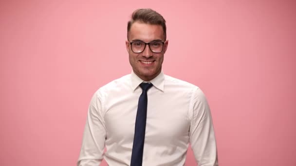 sexy jonge zakenman in wit shirt dragen bril glimlachen en wijzende vingers op roze achtergrond - Video