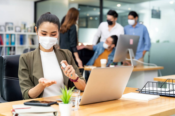 Asian office employee businesswoman wear protective face mask use alcohol spray hand sanitiser for hygiene in new normal office with social distance practice prevent coronavirus COVID-19 spreading. - Photo, Image