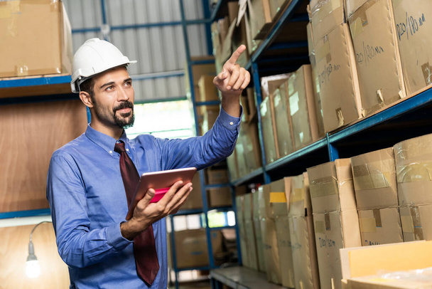 White caucasian middle east warehouse manager hold digital tablet to do inventory in warehouse distribution center environment.  For business warehouse inventory and logistic concept. - Foto, afbeelding