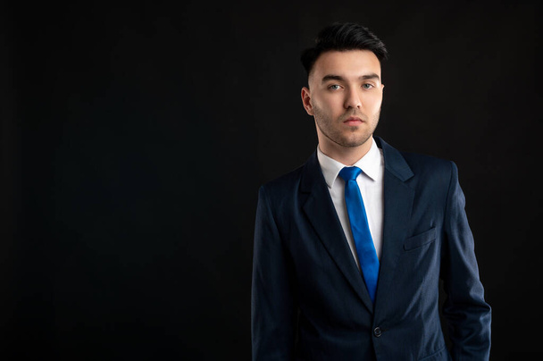 Portrait of business man wearing blue business suit and tie isolated on black background - 写真・画像