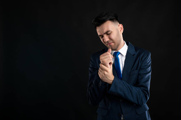 Portrait d'un homme d'affaires portant un costume d'affaires bleu et une cravate gesticulant des douleurs articulaires isolées sur fond noir avec espace de copie publicitaire - Photo, image