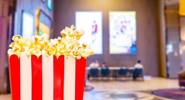Velká čtvercová pruhovaná krabice se slaným popcornem na filmovém pozadí. Koncept filmu - Fotografie, Obrázek