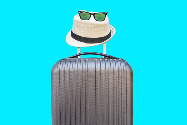 Sommerzeit - Schwarze Reisetasche und Strohhut mit Sonnenbrille auf blauem Hintergrund - Foto, Bild