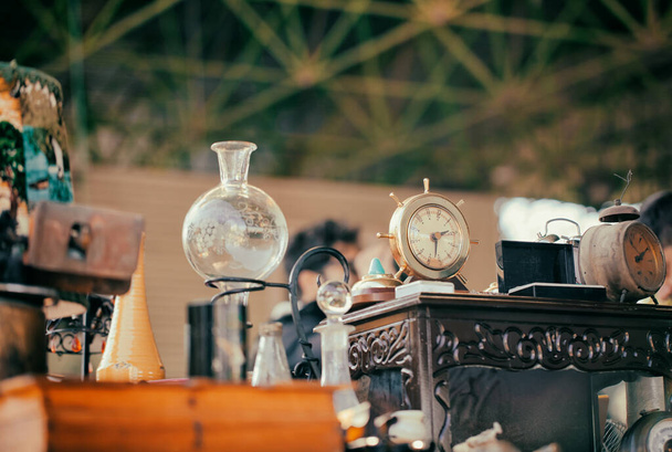 フリーマーケットでは、昔ながらの時計、花瓶、ランプシェード、ナイトスタンド。アンティークバザーでカウンター上のヴィンテージ家具 - 写真・画像
