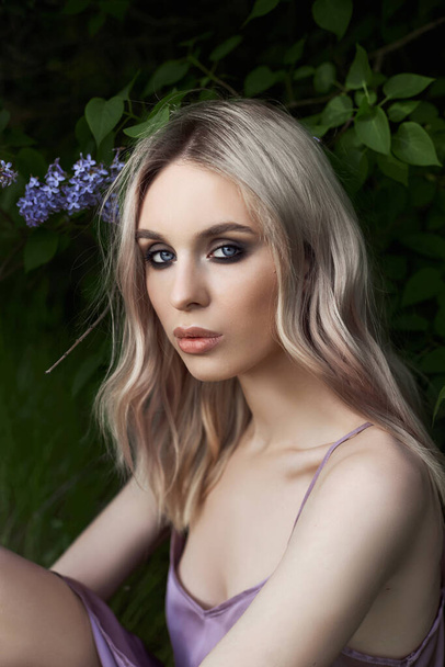 Portrait of a woman in lilac bushes in a purple dress. Face of a girl in lilac flowers close up - Photo, image