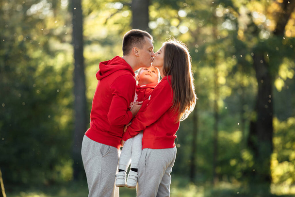 Мама, тато обіймає доньку і цілується в осінньому парку. Молода сім'я проводить час разом у відпустці, на відкритому повітрі. Концепція сімейного відпочинку. Мати, батько, день дитини
 - Фото, зображення