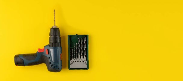 cordless drill, screwdriver with drill bit on yellow background,top view.Drill with drills of different types and sizes on a yellow background,flat lay - Photo, image