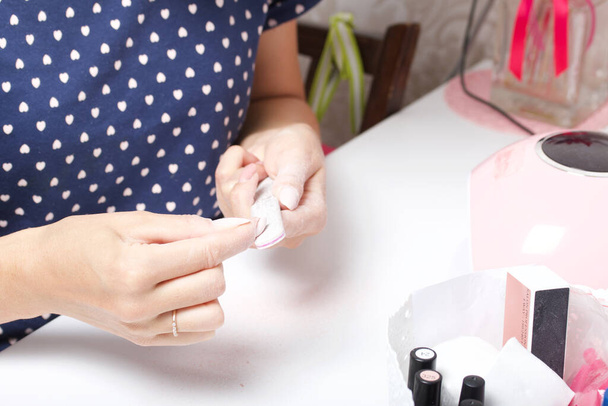 A woman makes her own manicure. Removes old nail Polish with a nail buff. Taken in close-up. - Фото, изображение