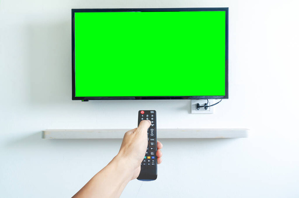 Hand houden van TV afstandsbediening over groen scherm een moderne televisie. Plaats voor uw advertentie. - Foto, afbeelding