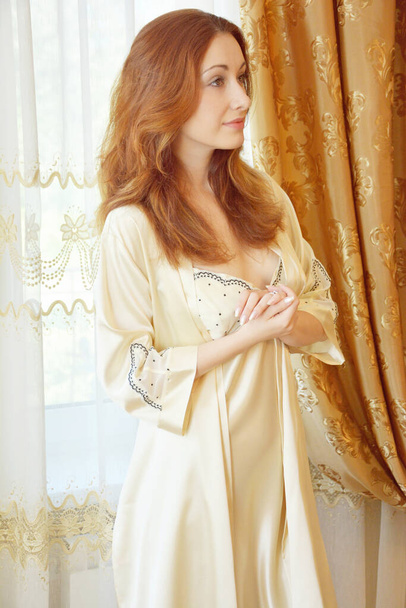 Woman in beige boudoir interior and silk golden robe, lingerie concept - 写真・画像