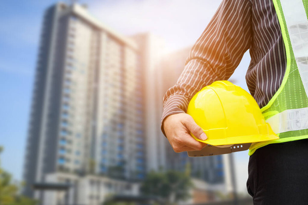 Asian business man construction engineer or architect worker with yellow protective helmet at large condominium building site - Photo, Image