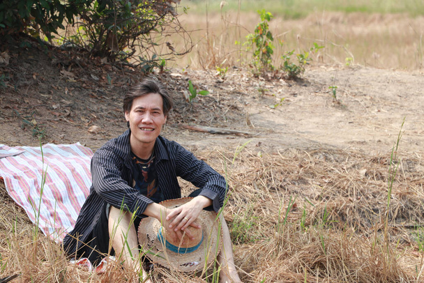 Agricoltore maschio utilizzare il perizoma sul pavimento per rilassarsi seduti e il cappello in mano sulla natura. - Foto, immagini