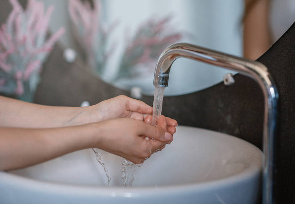 Onherkenbare jonge vrouw wassen handen in wastafel in de badkamer, close-up van handen - Foto, afbeelding