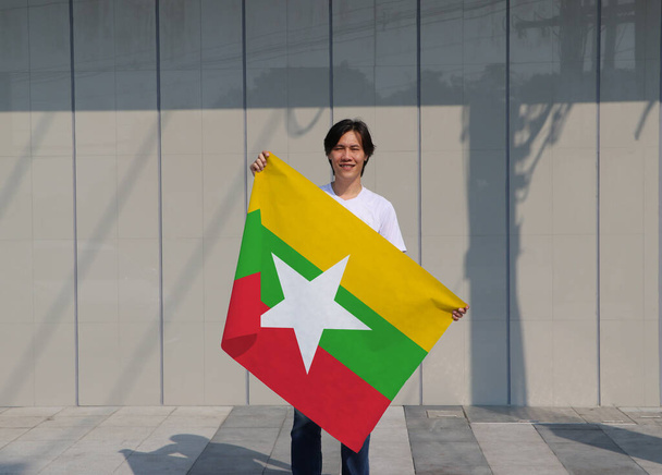 De man houdt Myanmar vlag in zijn handen op grijze achtergrond. - Foto, afbeelding