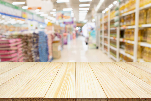 Holz Tischplatte Produktdisplay mit abstrakten Unschärfe Supermarkt Gang mit Reis in der Verpackung zum Verkauf und Pflanzenölflaschen in den Regalen Hintergrund - Foto, Bild