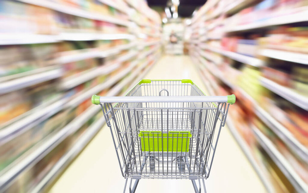 Supermarket aisle with empty green shopping cart in motion blur abstract background - Photo, Image