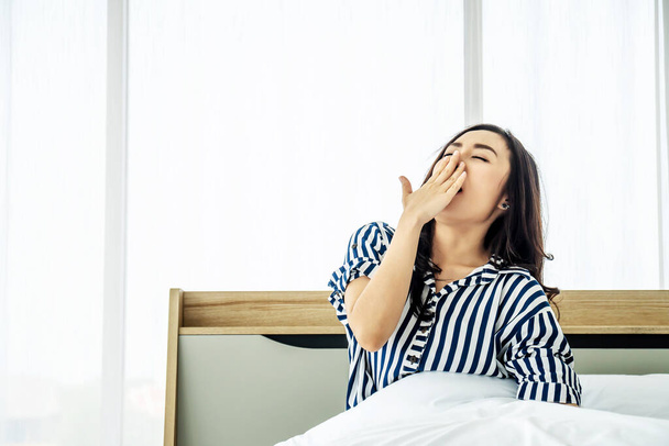 rest, holidays, comfort and people concept, Portrait of sleepy asian woman in sleepwear yawning after her waking up so early in the morning, Sitting on bed - Photo, Image