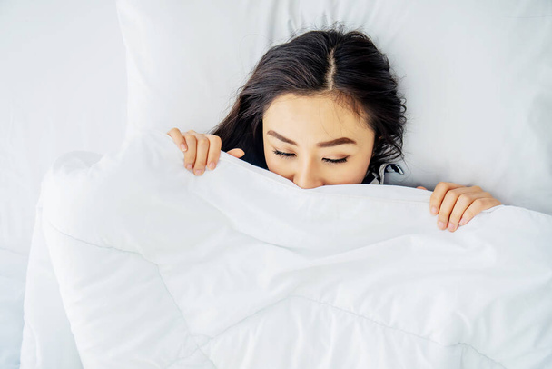 Top vista de dormir asiático mulher cobrir rosto com cobertor flat lay. Close-up de mulheres jovens, dormindo sob cobertor branco e cobrindo metade do rosto. Espaço de cópia para propaganda
 - Foto, Imagem