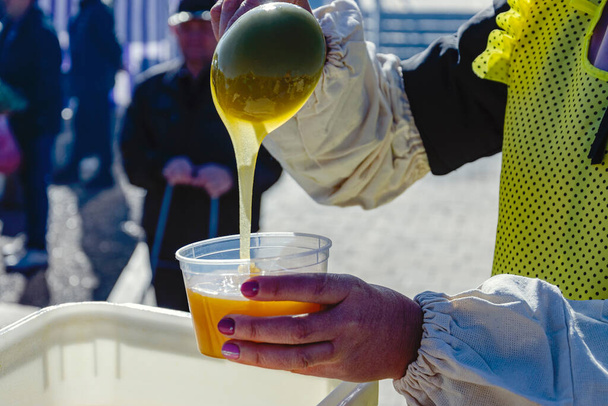 Una mujer pone miel de abeja en un recipiente de plástico usando un cucharón. - Foto, imagen