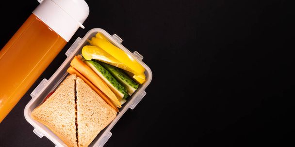 Сэндвич с хлебом и овощами в коробке для ланча рядом с бутылкой сока - вид сверху и копировальная площадка. Здоровый обед, растительный или вегетарианский обед, снятый сверху - Фото, изображение