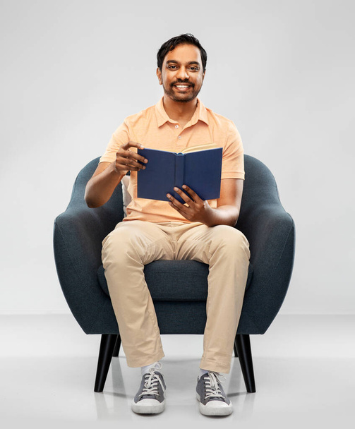 happy young indian man reading book in chair - Фото, изображение
