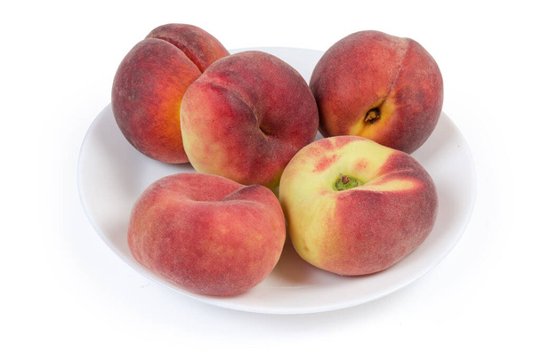 Flat and ordinary peaches lie on the white dish on a white background - Photo, Image