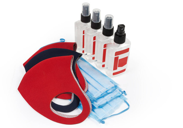 Gesichtsmasken aus elastischem Schutzgewebe, medizinische Einmalmasken und antiseptische Flaschen in Form von Spray auf weißem Hintergrund - Foto, Bild