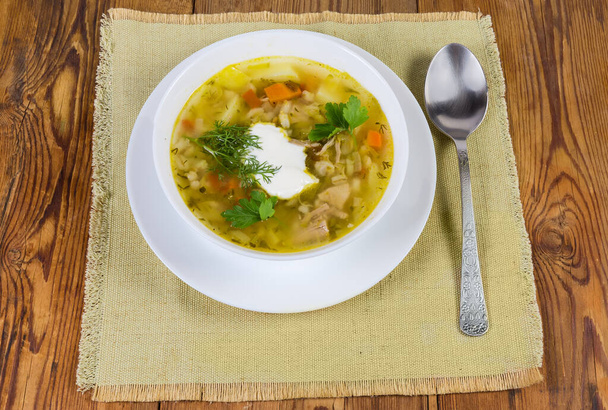 La porción rassolnik - la sopa de carne con la cebada perlada y los pepinos en vinagre sazonados con la crema agria, la cuchara echan a la servilleta sobre la mesa vieja rústica - Foto, imagen