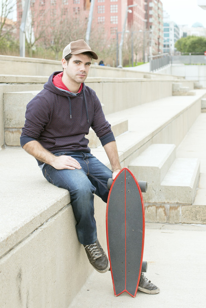 Человек сидит на улице со скейтбордом
. - Фото, изображение